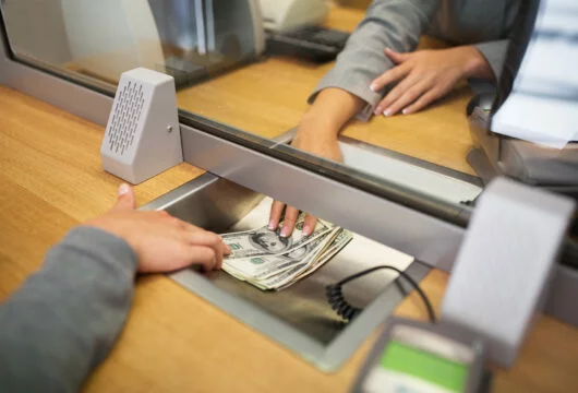 Teller handing cash to a customer through a partition at a bank counter