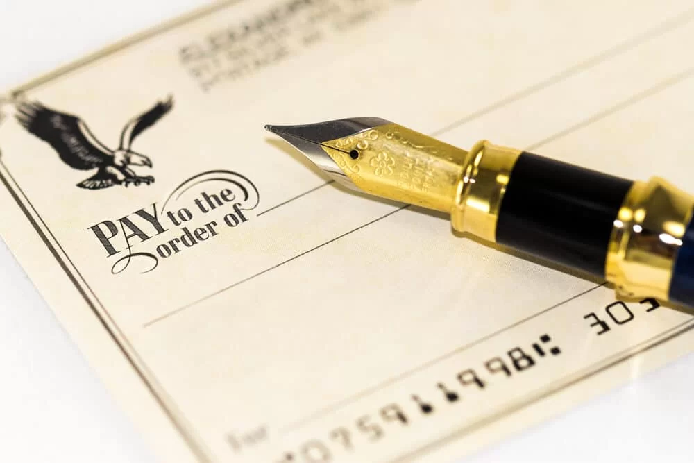 Close-up of a pen resting on the "Pay to the Order of" field of a blank check