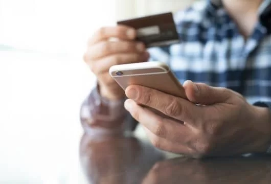 Man holding a cell phone and Netspend card while applying for a loan