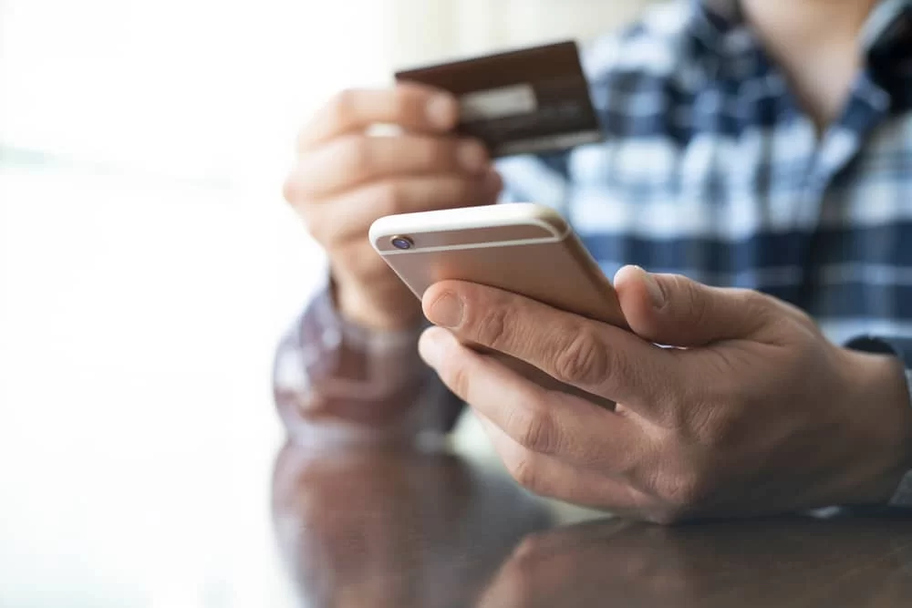 Man holding a cell phone and Netspend card while applying for a loan