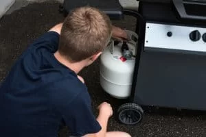 Young man connecting a propane tank to a grill after refilling it
