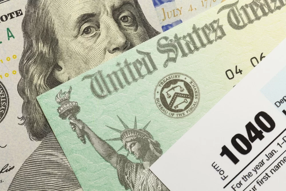 Tax refund check, 1040 form, and cash resting in a pile