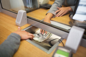 Teller handing cash to a customer through a partition at a bank counter