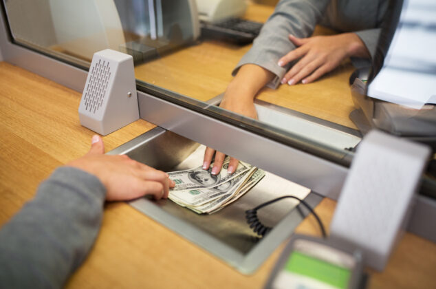 Teller handing cash to a customer through a partition at a bank counter