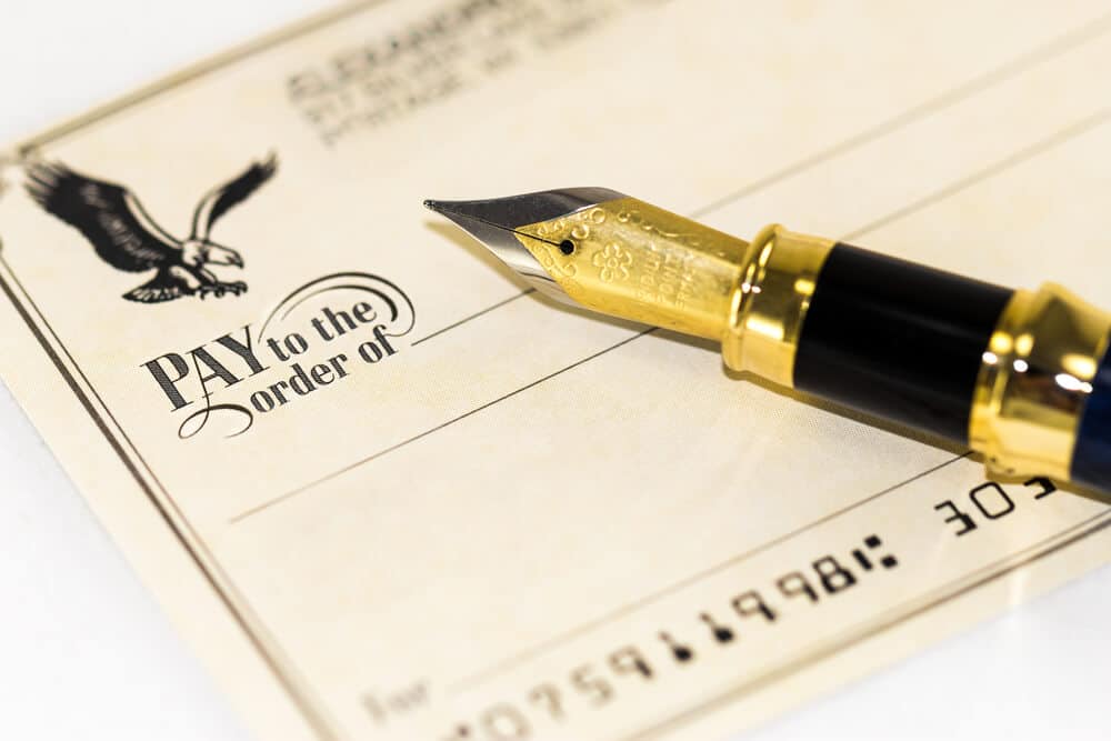 Close-up of a pen resting on the "Pay to the Order of" field of a blank check