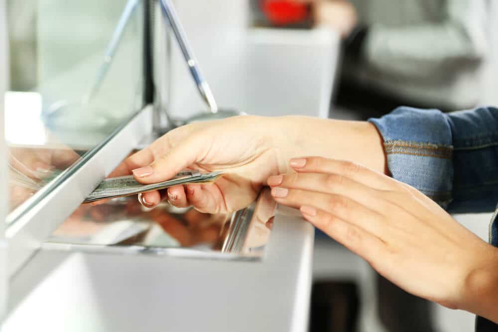 Hands passing cash to a teller to pay a check cashing fee