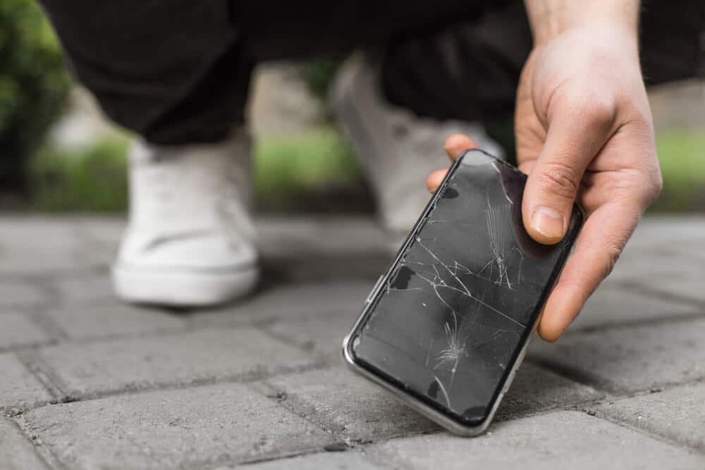 Man picking up a broken phone after dropping it on the ground