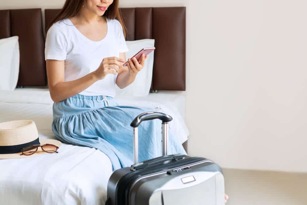 Young woman sitting on hotel room bed after checking in