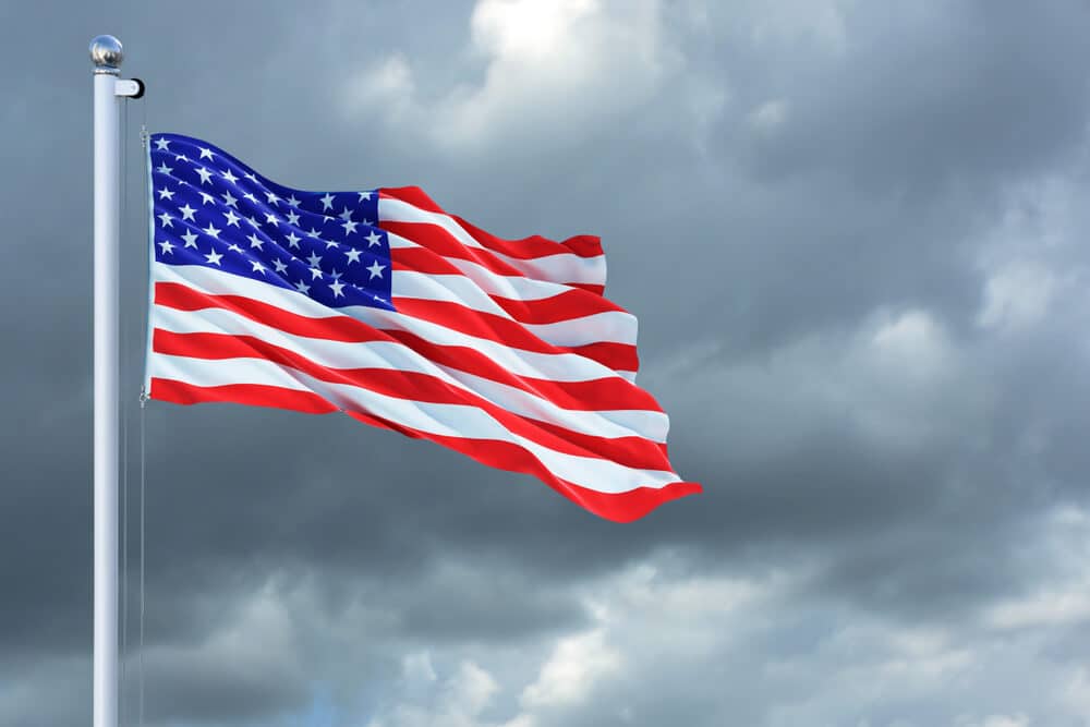 American flag waving on flag pole with cloudy sky