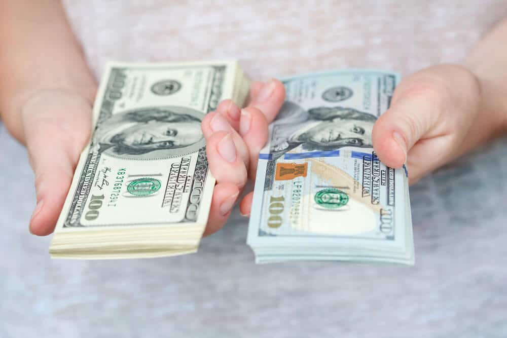 A woman holding two stacks of cash after cashing a check twice.