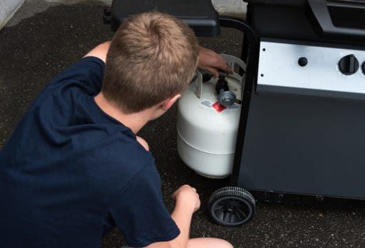 Young man connecting a propane tank to a grill after refilling it