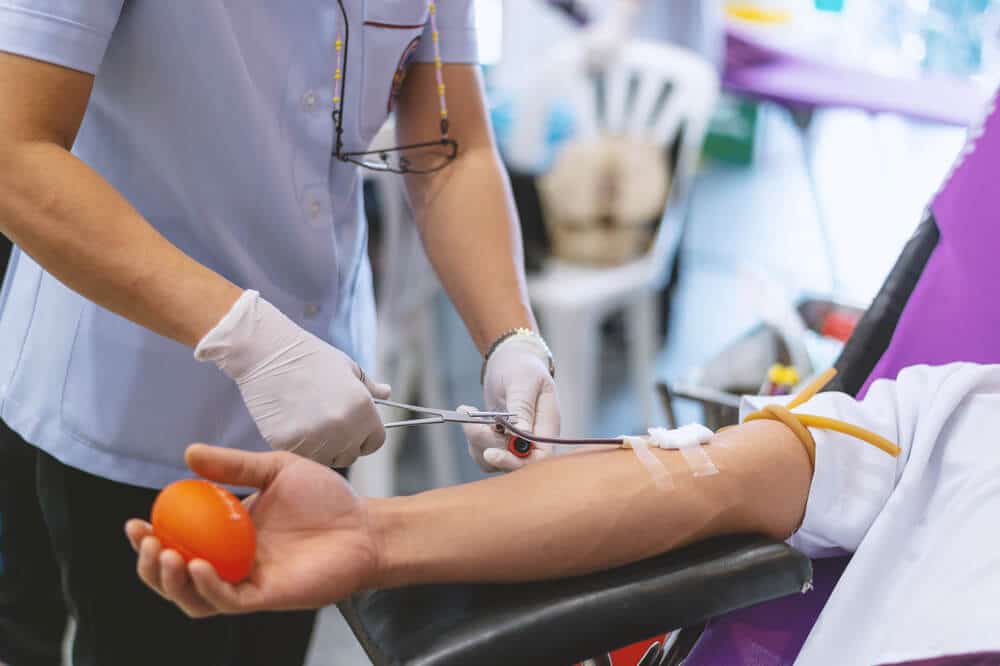 Woman adjusting tubing in donor's arm as donor prepares to give blood or plasma