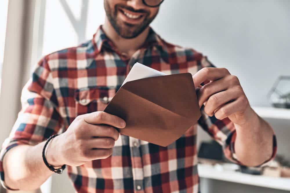 Man removing a printable gift certificate from a brown envelope