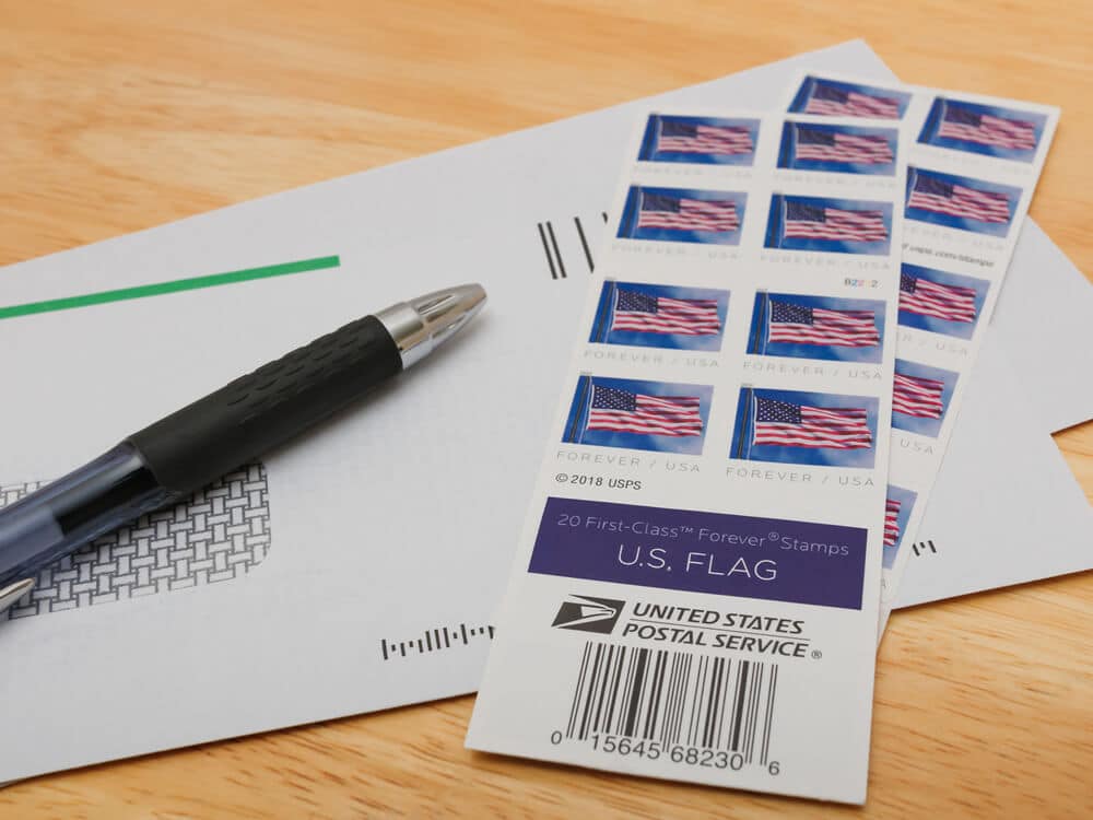 Pen, envelopes, and two sheets of stamps resting on a table