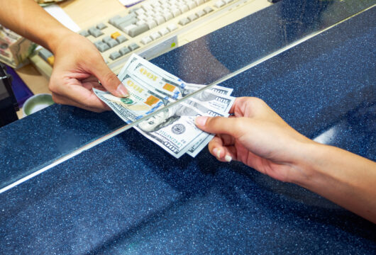 Close-up of a teller handing cash to someone after cashing a two-party check