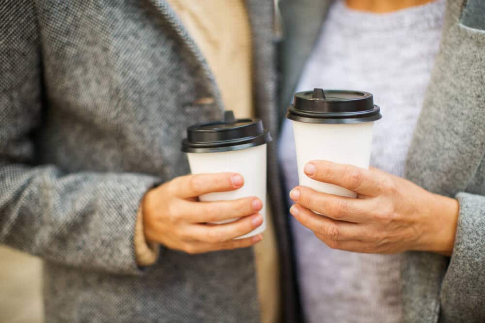 Two senior citizens stand with their cups of discounted coffee.