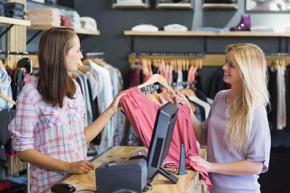 teen girl selling clothing to a young woman over a retail clothing store counter