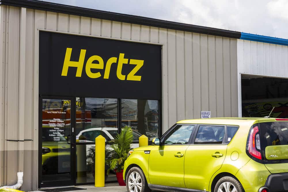 Hertz car rental storefront with a yellow car parked outside