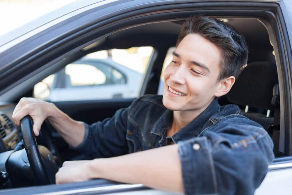 young man smiling while driving a rental car