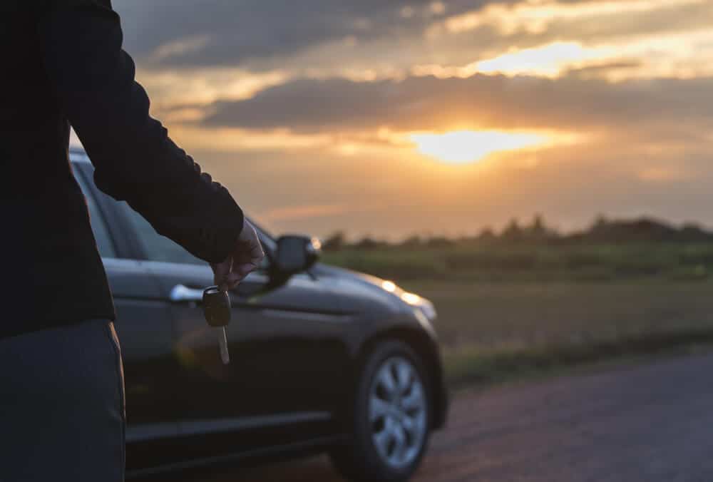 woman holding a car key in front of a car at sunset