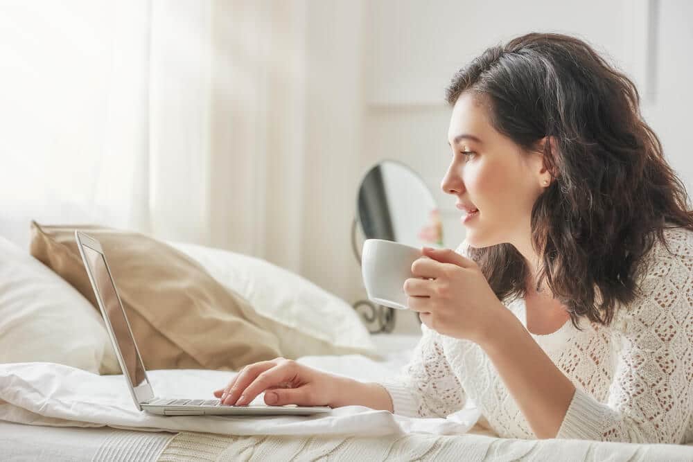 A woman sips coffee as she browsing the list of instant approval credit cards on her laptop.